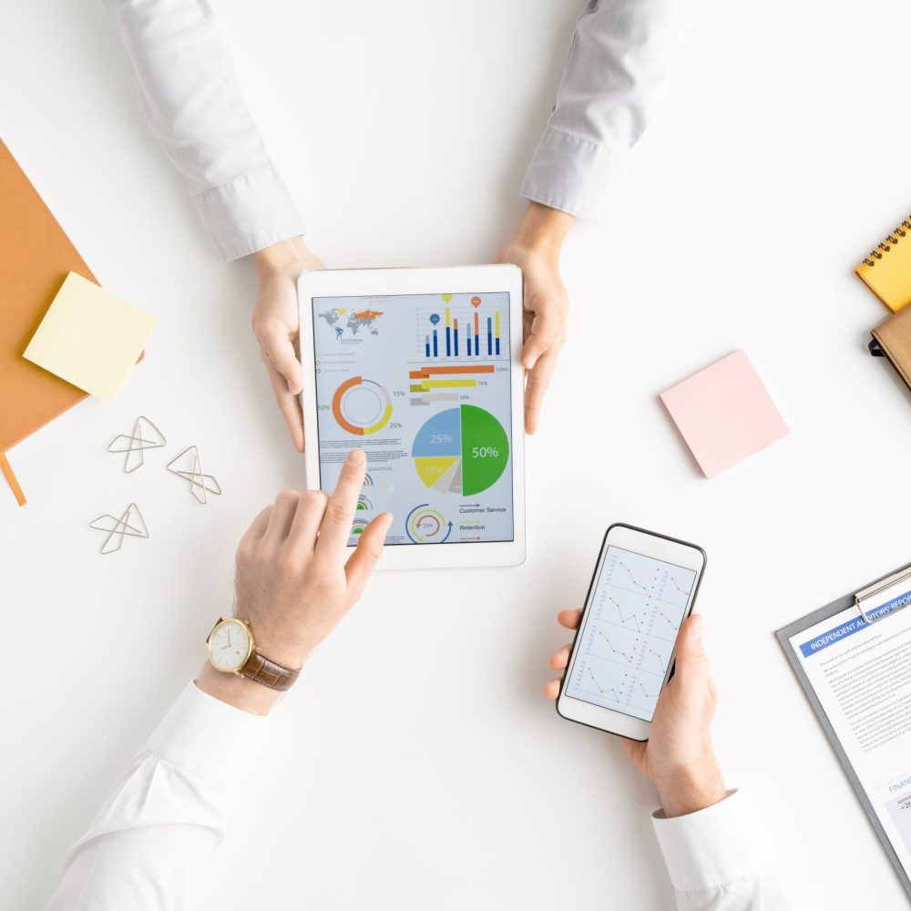 View of hands of analysts or brokers with gadgets discussing financial diagram View of hands of two analysts or brokers with gadgets discussing financial data on touchscreen while one of them pointing at circle diagram